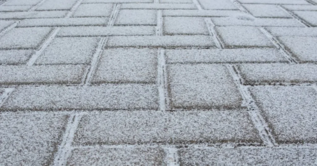 Close-up of rectangular concrete pavers dusted with a light layer of frost, showing the paver joint lines and texture